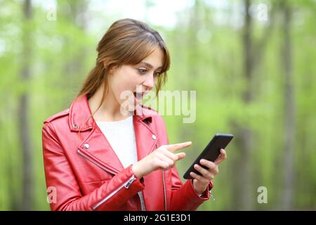 Une femme surprise consulte un smartphone dans une forêt verte Banque D'Images