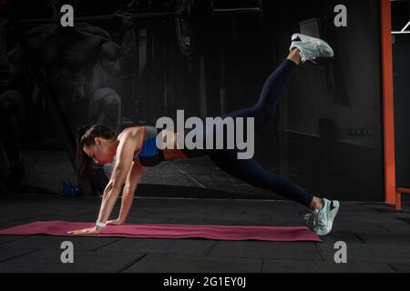 Fille exécutant la planche sur le devant sur les bras droits avec les jambes surélevés à la salle de gym Banque D'Images