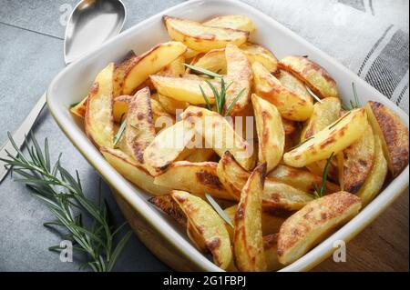 Pommes de terre rôties croustillantes aux feuilles de romarin fraîches dans un plat à pâtisserie sur fond gris. Banque D'Images