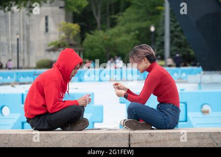 Un jeune homme et une jeune femme, tous vêtus de rouge, jouent à un jeu de cartes près de Unisphere à Flushing Meadow Corona Park dans Queens, New York. Banque D'Images