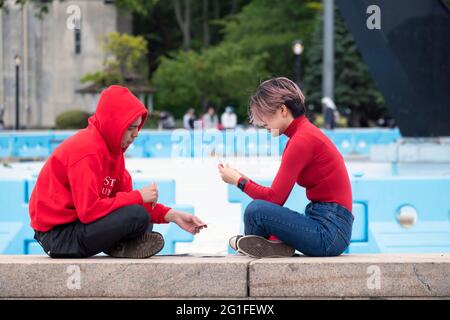 Un jeune homme et une jeune femme, tous vêtus de rouge, jouent à un jeu de cartes près de Unisphere à Flushing Meadow Corona Park dans Queens, New York. Banque D'Images