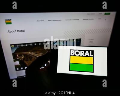 Personne tenant un téléphone portable avec le logo de la société australienne de matériaux Boral Limited à l'écran en face de la page Web d'affaires. Mise au point sur l'affichage du téléphone. Banque D'Images