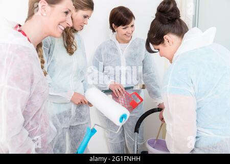 Groupe d'amis heureux de sexe féminin tenant de la peinture, du rouleau et du pinceau pour rénover la maison Banque D'Images