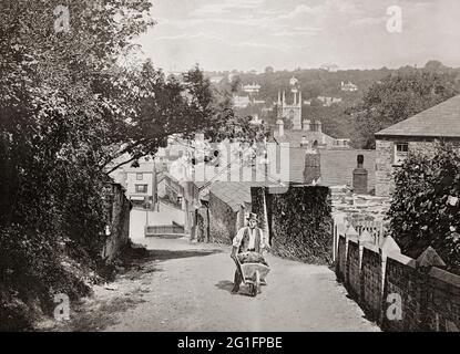 Vue de la fin du XIXe siècle d'un jardinier et d'une brouette qui monte sur une colline à Bodmin, une ville historique de Cornwall, en Angleterre. Au milieu de la distance peut être vu la tour de l'église normande du XVe siècle de St Petroc, en grande partie reconstruite et l'une des plus grandes églises de Cornwall. Banque D'Images