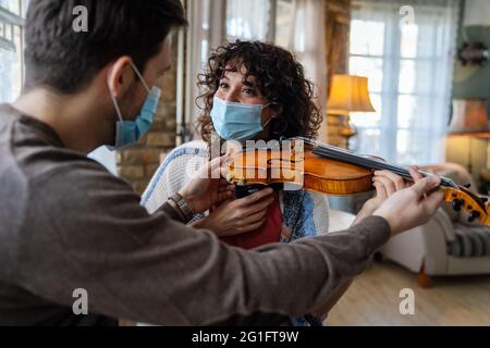 Une femme heureuse joue du violon sous les instructions d'un professeur de musique dans un masque pendant le coronavirus à la maison Banque D'Images