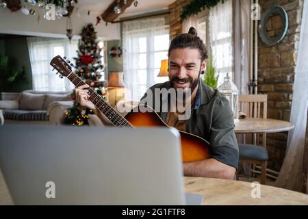 Jeune hispanique jouant de la guitare à la maison avec un ordinateur portable Banque D'Images