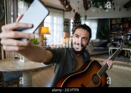 Jeune hispanique jouant de la guitare à la maison avec un ordinateur portable Banque D'Images