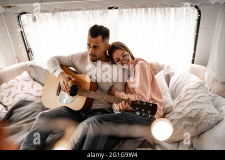 bonne femme embrassant petit ami jouant de la guitare en campeur Banque D'Images