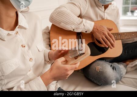 vue rognée d'un couple dans des masques médicaux jouant des instruments de musique à la maison Banque D'Images