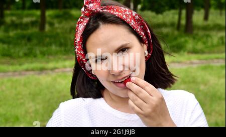 Fille mangeant fraise, souriant heureux, regardant l'appareil photo. Jeune femme mangeant des baies de fraises rouges. Portrait de maman, femme au foyer, fermier Banque D'Images