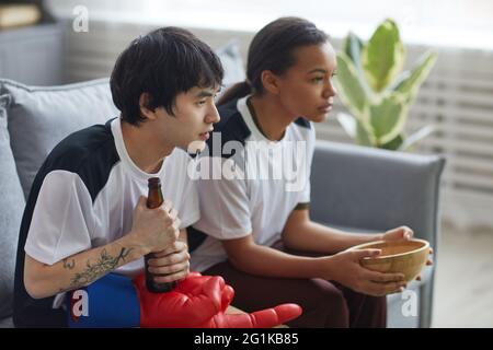 Vue latérale de deux jeunes regardant la télévision et de manger des en-cas à la maison, salle de copie Banque D'Images