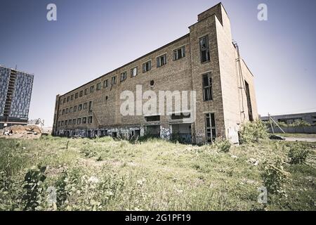 Bâtiment abandonné de plusieurs étages en brique rouge avec des fenêtres en verre cassées debout seul dans un champ herbacé. Une image en tons Banque D'Images