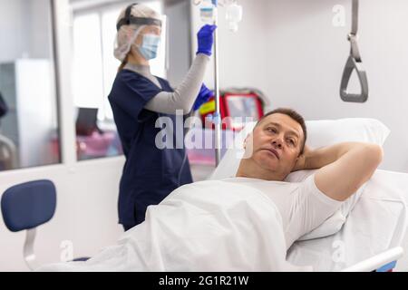 Patient adulte allongé sur le lit lors d'une injection intraveineuse en déposant une bouteille dans la clinique de l'hôpital Banque D'Images