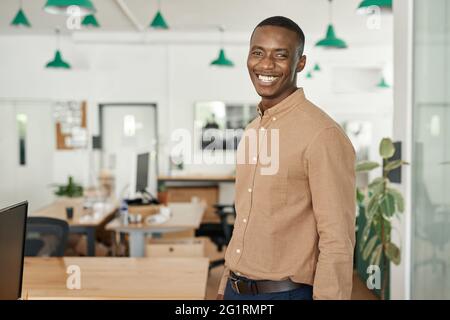 Rire un jeune homme d'affaires africain debout seul dans un bureau Banque D'Images
