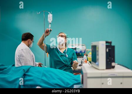 Anonyme medic contre infirmière en uniforme injectant du médicament dans le compte-gouttes au travail à l'hôpital sur fond d'aigue-marine Banque D'Images