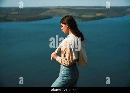 Jolie femme en tenue décontractée se tenant au sommet de la montagne près de la rivière Dniester. Femme attrayante bénéficiant d'une vue panoramique sur le paysage naturel de la région de Bakota. Banque D'Images