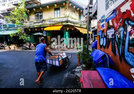 Un vendeur de nourriture de sexe masculin pousse son chariot le long d'une route étroite à Talat Noi, Bangkok, Thaïlande Banque D'Images