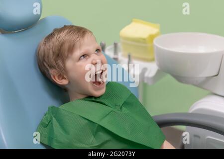 Drôle criant enfant en colère caucasien, a ouvert sa bouche et regarde le dentiste médecin dans la clinique dentaire, en attendant le traitement et l'hygiène buccale. Conc Banque D'Images