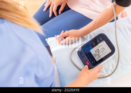 Jeune femme qui a vérifié sa tension artérielle par une infirmière, un médecin ou un visiteur de santé. Santé cardiaque. Moniteur de la jauge numérique de la pression artérielle. Banque D'Images