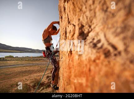 Jeune athlète femme escalade sur le mur plat de la roche au coucher du soleil près de la rivière au Kazakhstan Banque D'Images