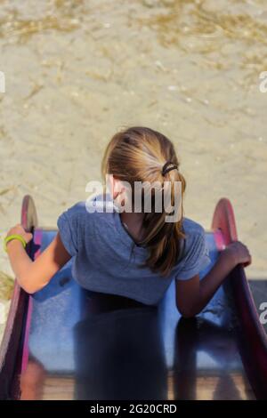 Déconcentrer l'expression d'émotion la jeune fille glisse en bas de la colline sur le terrain de jeu. Colline bleu et rouge vif pour enfants. Jeu d'été en famille. Vue de l'arrière. Vertica Banque D'Images