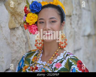 Jeune femme mexicaine belle avec maquillage porte la traditionnelle Yucatecan Yucatecan robe folklorique avec des fleurs dans ses cheveux et sourit pour l'appareil photo. Banque D'Images