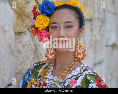 Jeune femme mexicaine belle avec maquillage porte traditionnelle Yucatecan Yucatecan robe folklorique avec des fleurs dans ses cheveux et pose pour la caméra. Banque D'Images