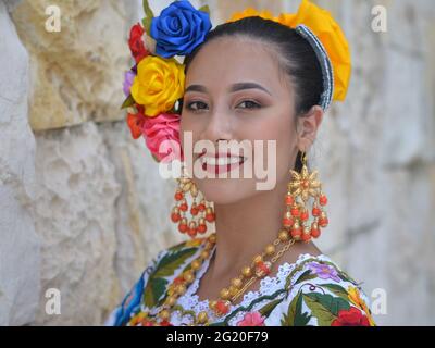 Jeune femme mexicaine belle avec maquillage porte la traditionnelle Yucatecan Yucatecan robe folklorique avec des fleurs dans ses cheveux et sourit pour l'appareil photo. Banque D'Images