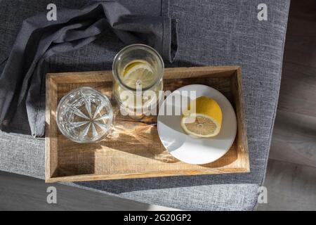 Un verre rafraîchissant d'eau, une bouteille d'eau et une tranche de citron sur un plateau, une serviette en lin, et un demi-citron sur une soucoupe à manger sur le canapé dans le Banque D'Images