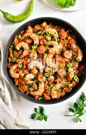 Vue rapprochée de jambalaya créole avec riz, saucisses fumées, viande de poulet et légumes dans une poêle sur fond de pierre blanche. Vue de dessus, plan d'appartement Banque D'Images