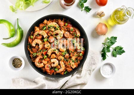 Jambalaya créole avec riz, viande de poulet, saucisses fumées et légumes dans une poêle sur fond de pierre blanche. Vue de dessus, plan d'installation, gros plan Banque D'Images