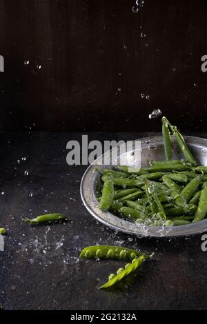 gousses de pois sur fond marron avec pulvérisation et éclaboussures d'eau. Banque D'Images