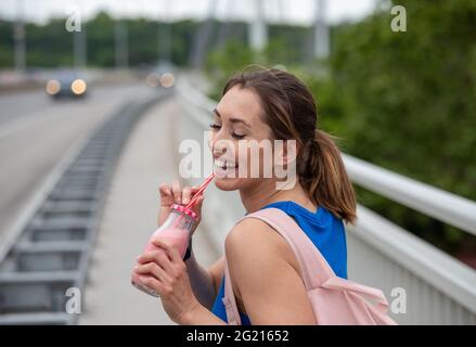 Jeune femme sportive marchant boire un milkshake à la fraise. Portrait d'une fille sur le pont après l'entraînement. Banque D'Images