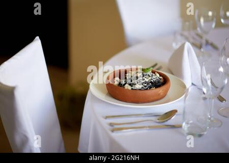 Spaghetti Al Nero Di Seppia avec tomates et herbes dans une plaque en céramique dans une salle à manger publique, avant et arrière-plan Banque D'Images