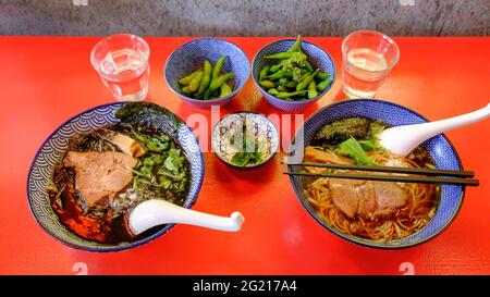 Photo de deux bols de ramen (soupe chaude japonaise) servis dans de beaux bols peints en bleu sur une table rouge vif. Banque D'Images