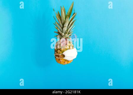 Ananas en rose lunettes de soleil masque médical sur fond bleu d'été. Ananas fruit visage drôle dans le masque protecteur dans le verrouillage du coronavirus covid Banque D'Images