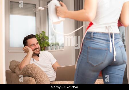 Jeune couple en appartement travaillant à faire des tâches. Homme penché sur le coude souriant. Femme tenant la main batteur cuisine. Banque D'Images