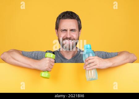 joyeux barbu homme derrière le papier tenir la barbell de fitness et bouteille d'eau pour l'entraînement sur place, la santé. Banque D'Images