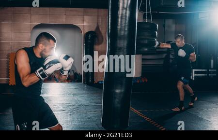 Muscle à l'aide d'un jeune boxeur sac de frappe dans une salle de sport. Boxer hitting punching bag de vitesse Banque D'Images