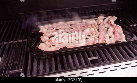 Cuisson de tranches de bacon sur un barbecue à gaz extérieur. Banque D'Images