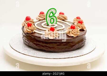 Gâteau d'anniversaire au chocolat avec bougie sous la forme du numéro six. Gâteau maison décoré de crème au chocolat et de cerises sur fond blanc Banque D'Images