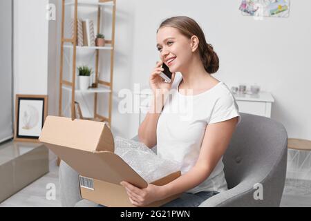 Belle jeune femme avec colis parlant par téléphone portable à la maison Banque D'Images