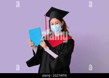 Une étudiante diplômée en masque de protection et avec livre sur fond de couleur Banque D'Images