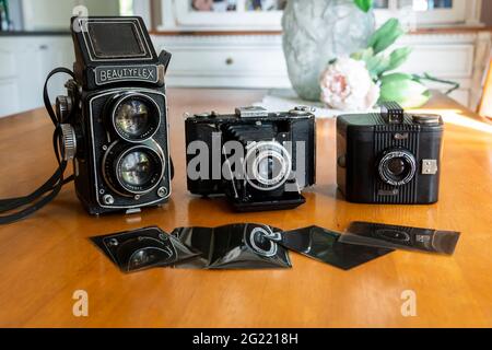 Trois appareils photo rétro vintage, un Beautyflex, un Zeiss et un Bullseye, sur une table en pin avec des négatifs photographiques dans une maison. Banque D'Images