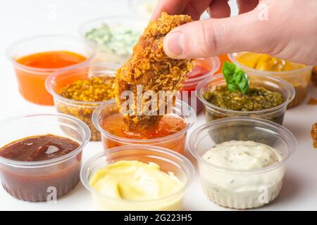 Trempez à la main une aile de poulet dans une tasse de ketchup Banque D'Images