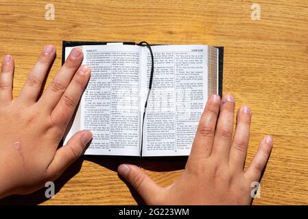 Les mains des enfants tiennent une bible penchée sur une table en bois. Petit livre Sainte Bible.Kid lecture de la sainte bible,closeup. Banque D'Images