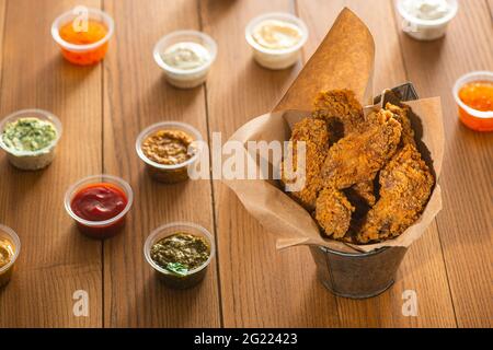 Seau d'ailes de poulet et sauces assorties dans de petites tasses sur table en bois Banque D'Images