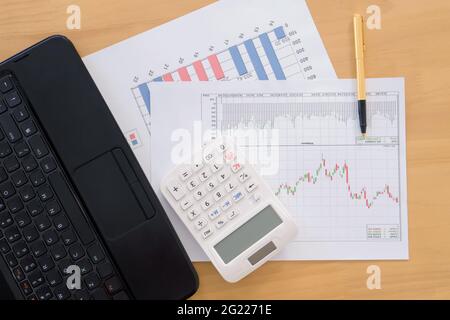 Différents tableaux financiers sur la table avec un ordinateur portable, une calculatrice et stylo Banque D'Images