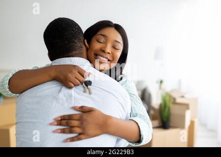 Concept de propriété de la maison. Femme noire excitée tenant la clé de la maison et embrassant son mari, espace libre Banque D'Images