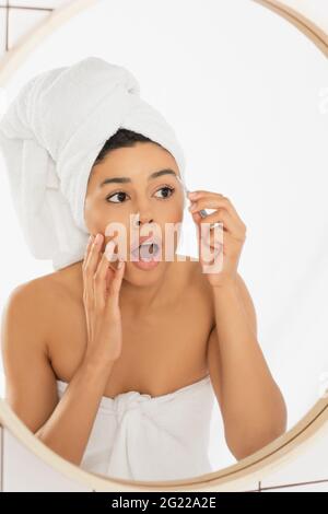 une jeune femme afro-américaine effrayée avec une bouche ouverte pleurs sourcils avec des pinces dans la salle de bains Banque D'Images